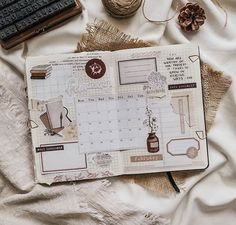 an open planner sitting on top of a bed next to some yarn and other items