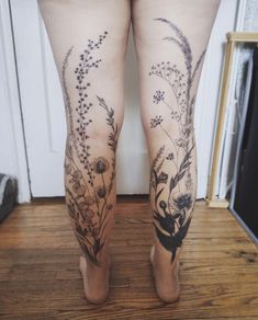 a woman's legs with flowers and plants tattooed on the thighs, standing in front of a door