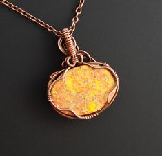 a necklace with an orange stone in the center on a chain that is attached to a black surface