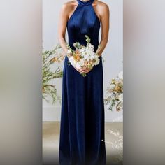 a woman in a long blue dress holding a white bouquet and wearing a halter top