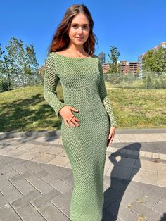 a woman in a green knitted dress poses for the camera on a brick walkway