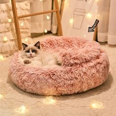 a cat is laying in a fluffy pink bed on the floor with fairy lights around it