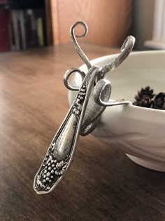 a silver spoon sitting on top of a wooden table next to a bowl filled with pine cones