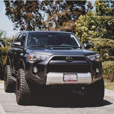 the front end of a black toyota 4runner on a road with trees in the background