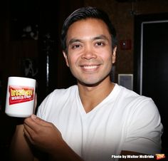 a man holding up a white cup in his right hand and smiling at the camera