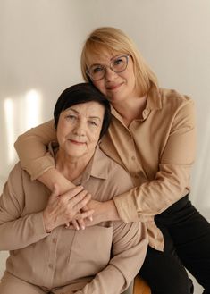 an older woman sitting on top of a wooden chair next to a younger woman who is wearing glasses