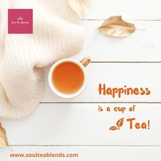 there is a cup of tea next to some leaves on the white wooden table with an inscription that says, happiness is a cup of tea