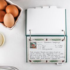 an open recipe book next to eggs and utensils on a white counter top