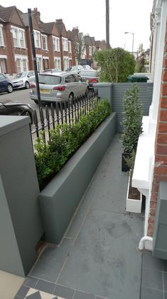 an outdoor patio area with plants and benches on the side of the building, along with cars parked in the street