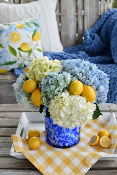 a blue vase filled with white and yellow flowers on top of a wooden table next to lemons