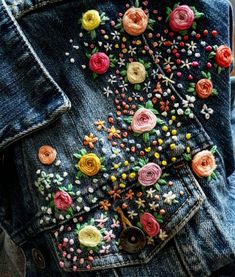 someone is wearing a jean jacket with colorful flowers on the pocket and buttons attached to it