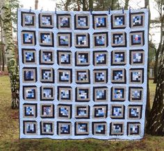 a blue and black quilt hanging from a tree in the grass with trees behind it