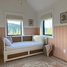 a white day bed sitting in the corner of a room with two windows and a rug on the floor