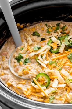 a crock pot filled with soup and topped with cheese, jalapenos, cilantro, and green peppers