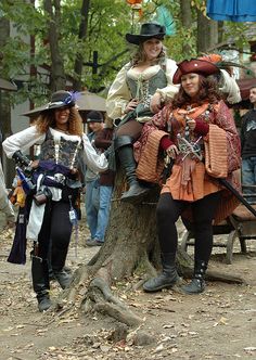 two women dressed in pirate costumes sitting on an elephant at the park while others look on