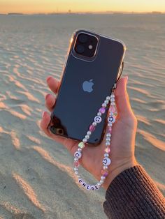 a person holding an iphone in their hand on the beach at sunset with beaded bracelets