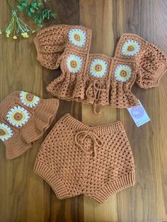 three crocheted diapers and two bonnets on a wooden table next to flowers