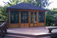 a wooden gazebo sitting on top of a lush green field next to a forest