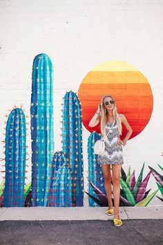 a woman standing in front of a cactus wall with sunglasses on her head and a handbag