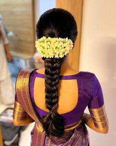 a woman with flowers in her hair is seen from the back, wearing a purple saree