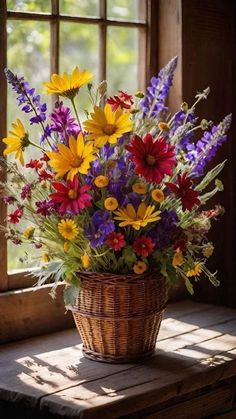 a basket filled with lots of colorful flowers sitting on top of a wooden table next to a window