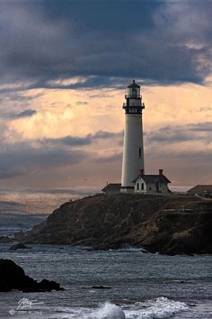 a light house sitting on top of a rocky cliff next to the ocean under a cloudy sky