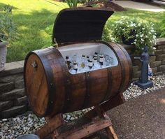 a wooden barrel filled with lots of bottles sitting on top of a stone wall next to a garden