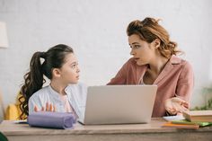 two women sitting at a table looking at a laptop