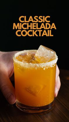 a hand holding a glass filled with an orange cocktail