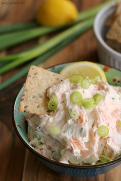 a bowl full of dip with crackers and lemon wedges