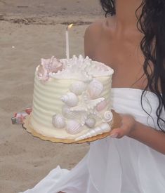 a woman holding a cake with seashells on it and a lit candle in the middle