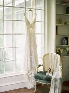 a wedding dress hanging on a window sill in front of a chair with a veil draped over it