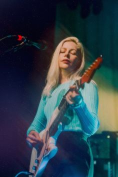 a woman holding a guitar while standing in front of a microphone