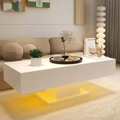 a modern living room with white furniture and yellow lighting on the coffee table in front of the couch