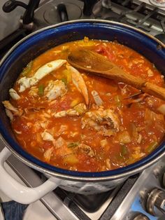 a blue pot filled with lots of food on top of a gas stove next to a wooden spoon