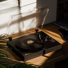 a record player sitting on top of a wooden table next to a plant and window