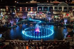 an aerial view of a fountain at night with people standing around it and lights on the water