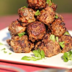 a pile of meatballs sitting on top of a white plate with green garnish