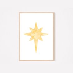 a watercolor painting of a yellow star on white paper with a wooden frame against a wall