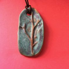 a ceramic pendant with a tree on it sitting on a red table next to a black bead necklace