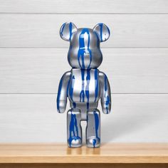 a silver and blue bear sitting on top of a wooden table next to a white wall