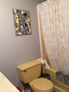 a yellow toilet sitting next to a bath tub in a bathroom under a painting on the wall