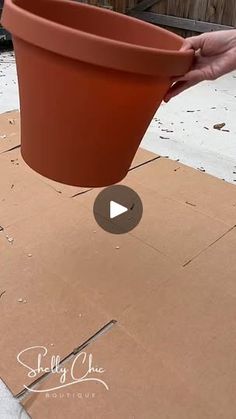 a person is holding a clay pot over a piece of cardboard that has been placed on the ground