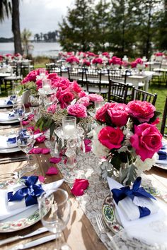 a long table is set with pink and white flowers in vases, plates and silverware