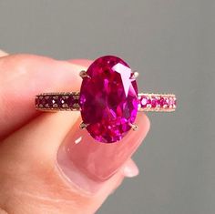 a woman's hand holding a ring with a large pink stone in the middle