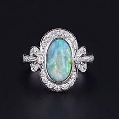 Opal and Diamond Ring: Experience the timeless beauty of this semi-black opal elegantly encased in 18k white gold and adorned with sparkling diamonds. The face of the 1990s ring measures 0.75 inches by 0.5 inches wide, and it is in great condition.  The ring is a size 6.5, but it can be resized free of charge. Your ring will arrive elegantly packaged, ready for gifting or as a special treat for yourself. Each piece is carefully wrapped to ensure a delightful unboxing experience. We also offer fr Luxury White Gold Opal Ring, Elegant Opal Ring With Center Stone, Art Deco Oval Opal Ring, Art Deco Style Oval Opal Ring, Elegant Opal Ring With Diamond Accents, Exquisite Multi-stone Opal Ring For Formal Occasions, Formal Multi-stone Opal Ring With Diamonds, Formal Multi-stone Diamond Opal Ring, Formal Oval Opal Ring With Diamonds