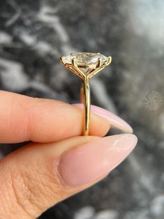 a woman's hand holding a yellow gold ring with an oval shaped diamond on it