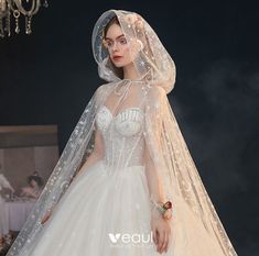 a woman in a white wedding dress with a veil on her head is standing next to a chandelier