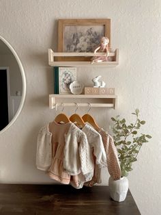 some baby clothes are hanging on a shelf next to a potted plant and mirror