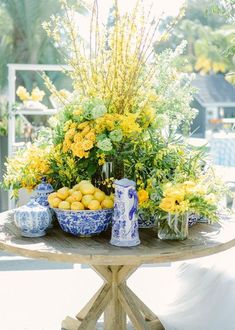 a table topped with blue and white vases filled with flowers next to lemons